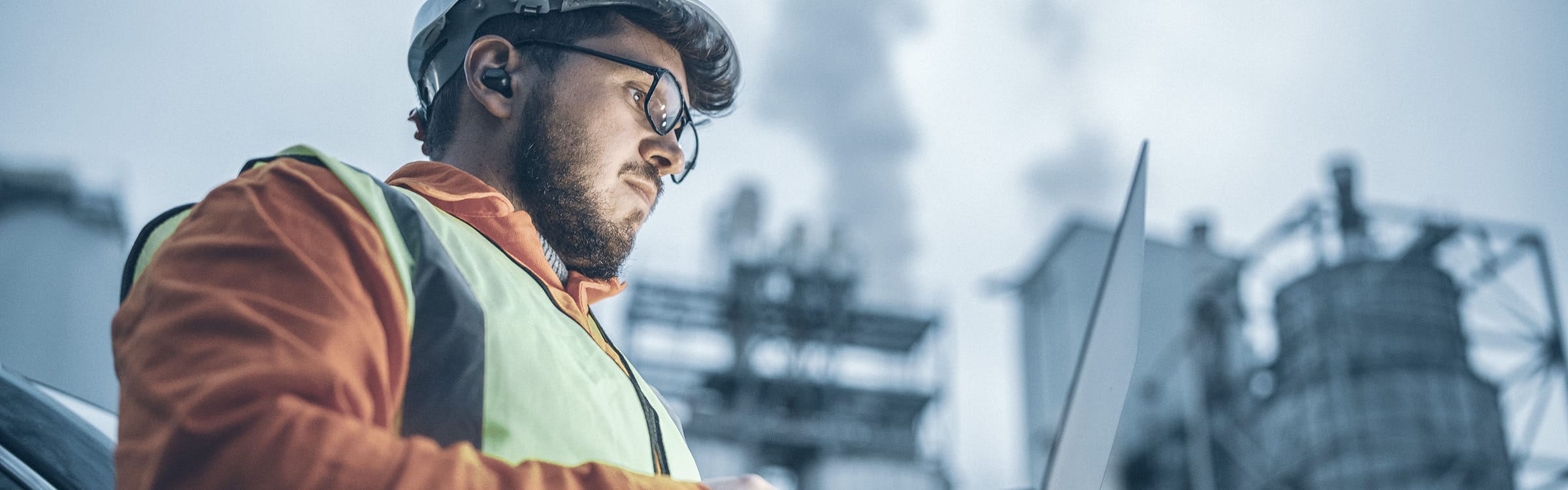 Mann mit Brille, Helm und Schutzweste bedient Laptop auf Fabrikgelände | GWM – Gesellschaft zur Weiterverwendung von Mineralstoffen – des Kreis Unna.