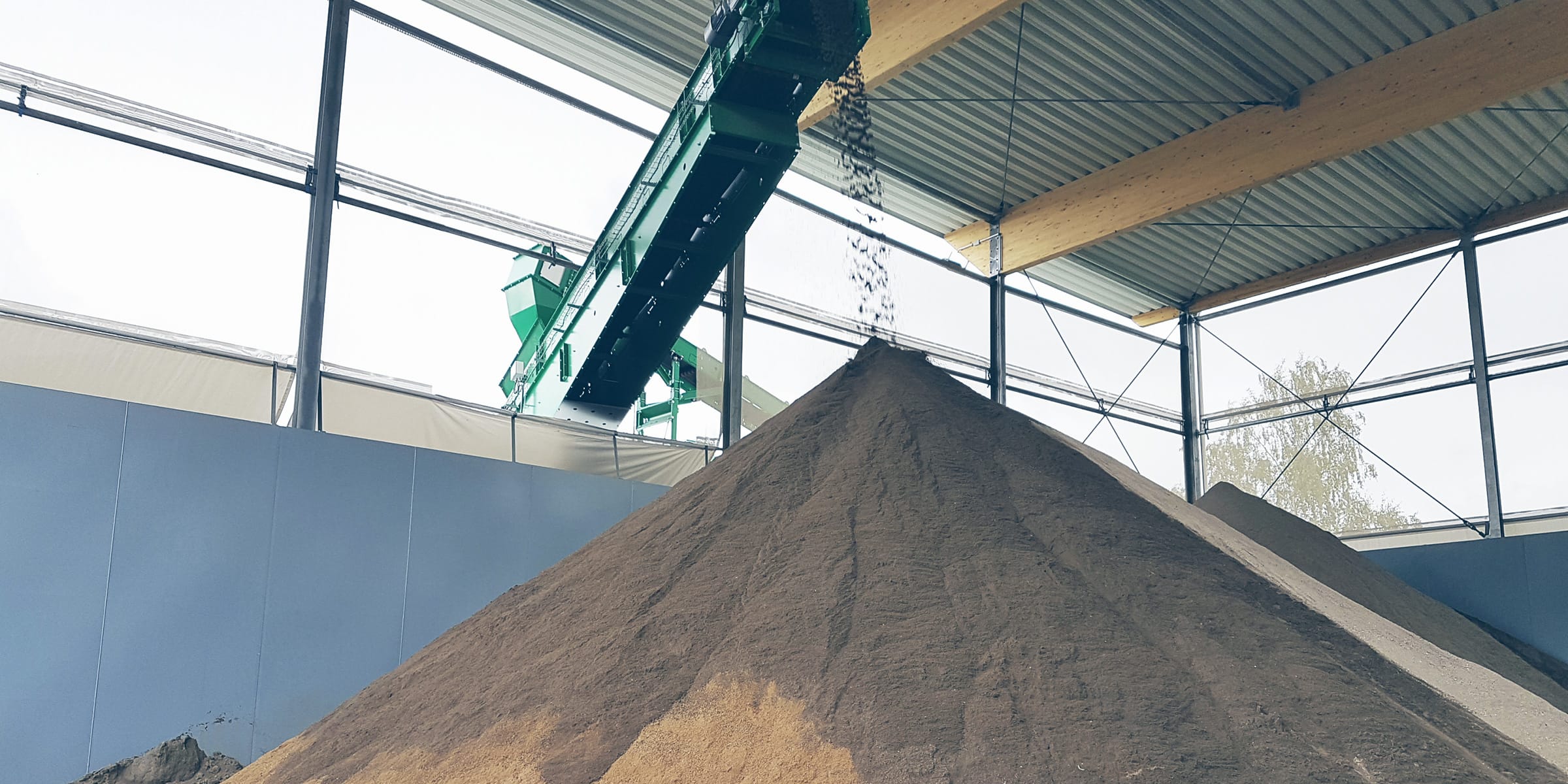 Sand fällt in Lagerhalle von Transportband auf Sandhaufen | Nachhaltige Sandproduktion bei der GWM – Gesellschaft zur Weiterverwendung von Mineralstoffen – des Kreis Unna.